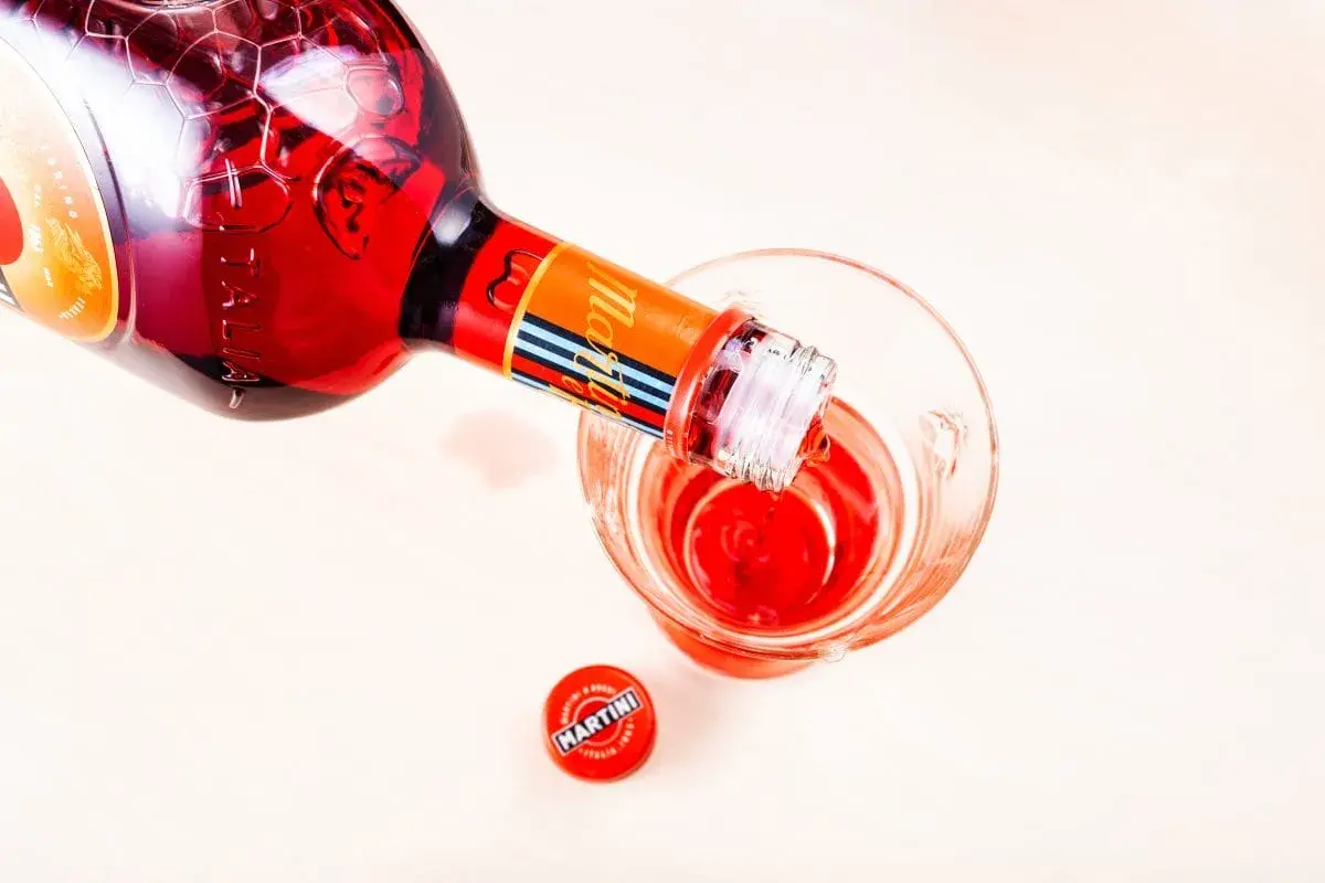 Czerwony Martini Fiero drink nalewany z butelki do szklanki. Obok leży czerwona zakrętka.