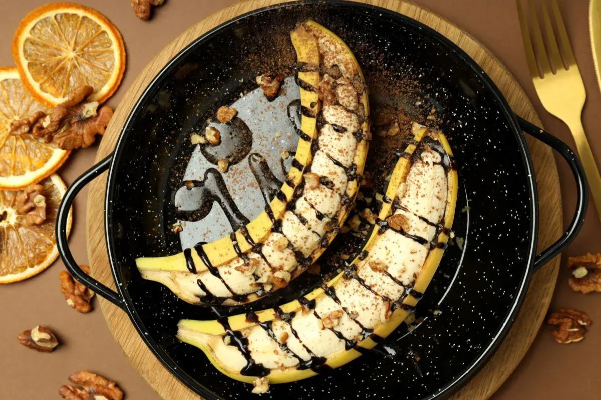 Szybki deser z bananów: połówki bananów zapieczone z orzechami, polane czekoladą i posypane kakao.