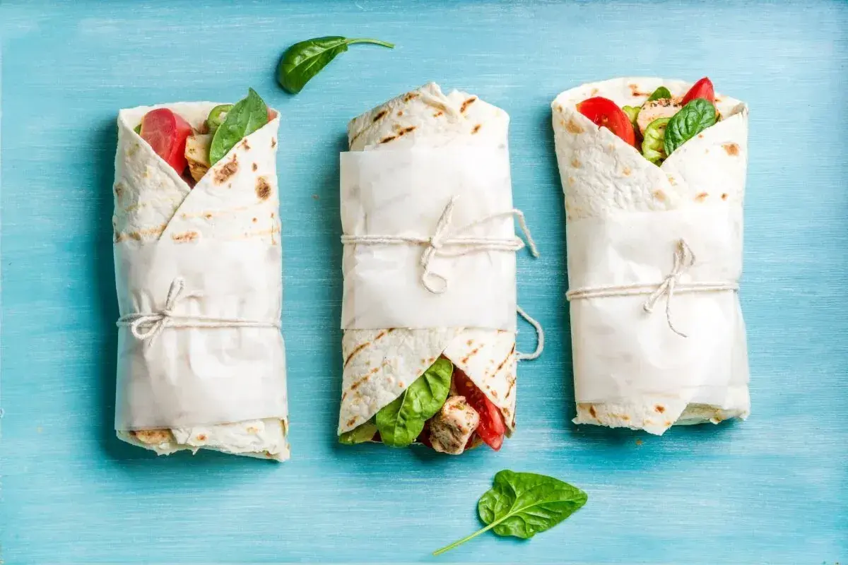 Trzy tortille zawinięte w papier, z widocznym nadzieniem z kurczaka, pomidorów i szpinaku. Idealne na keto tortilla przepis.