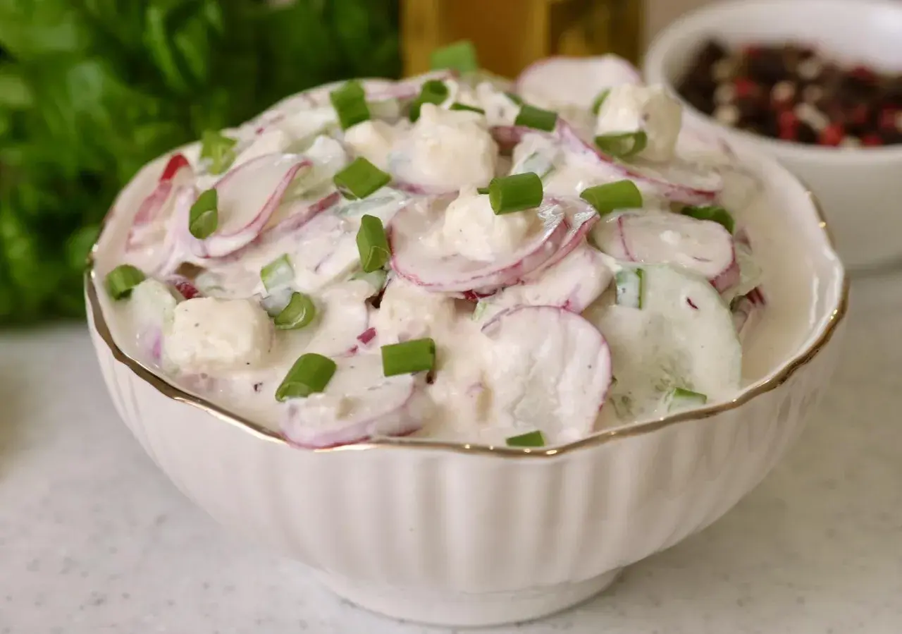 Rewelacyjna sałatka na grilla z rzodkiewką, ogórkiem i serem feta w kremowym sosie, posypana szczypiorkiem. Idealna na letnie przyjęcia.