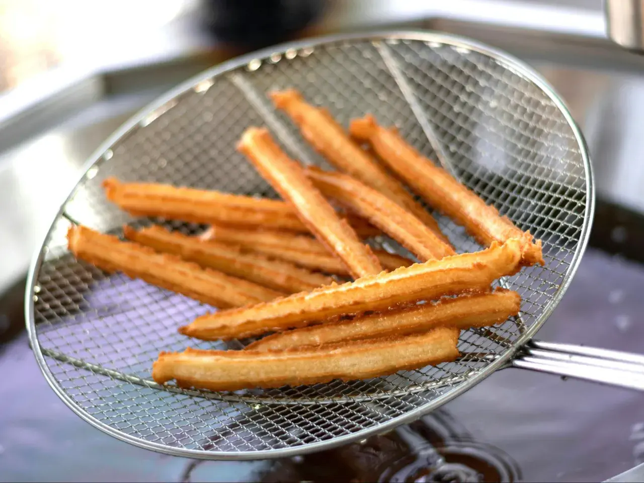 Złociste churros na sicie, właśnie wyjęte z gorącego oleju. Pytasz churros co to? To pyszny, smażony przysmak!