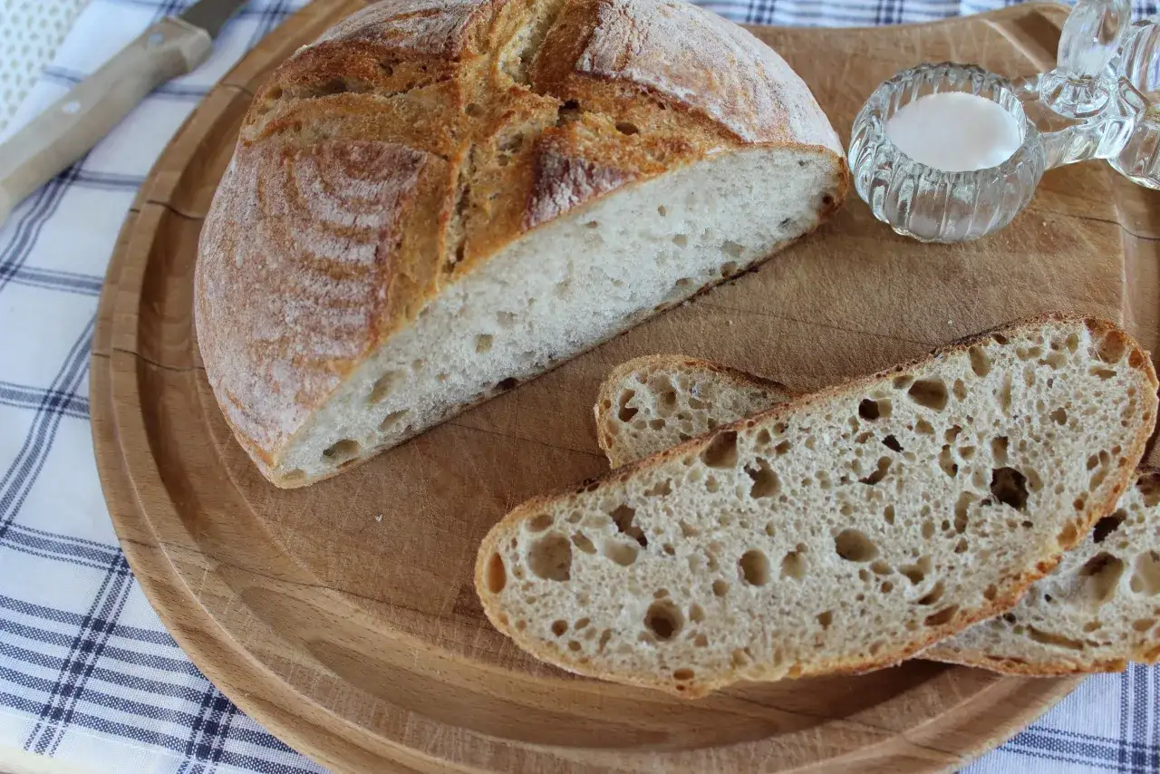 Chleb pszenno żytni na zakwasie, pokrojony na desce, z solniczką i nożem w tle.