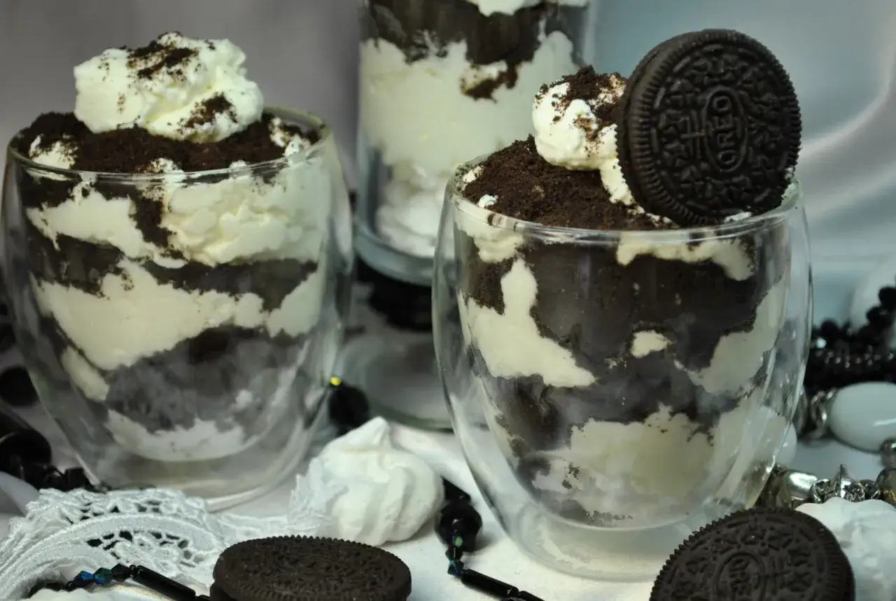 Warstwowe desery z kremem i pokruszonymi ciastkami Oreo, ozdobione całą ciastkiem. Pyszne Oreo ciastka w nowej odsłonie.
