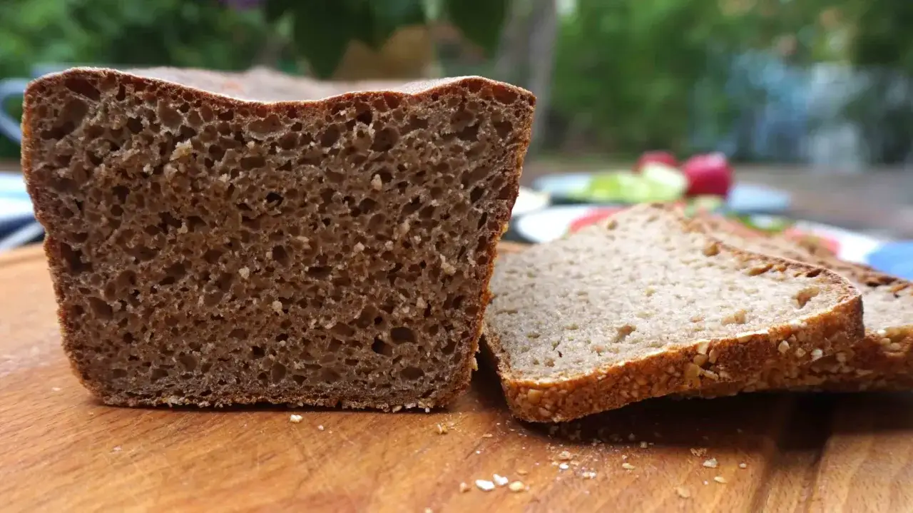 Kromka ciemnego chleba z niskim ig, obok leżą plastry tego samego pieczywa. Na drewnianej desce widać okruchy.