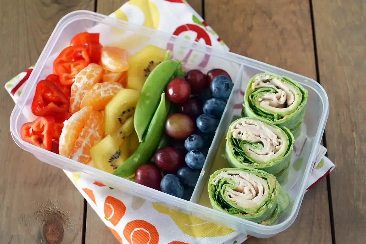 Kolorowy lunchbox z owocami, warzywami i roladkami z tortilli. Idealne zdrowe przekąski dla dzieci na wynos.