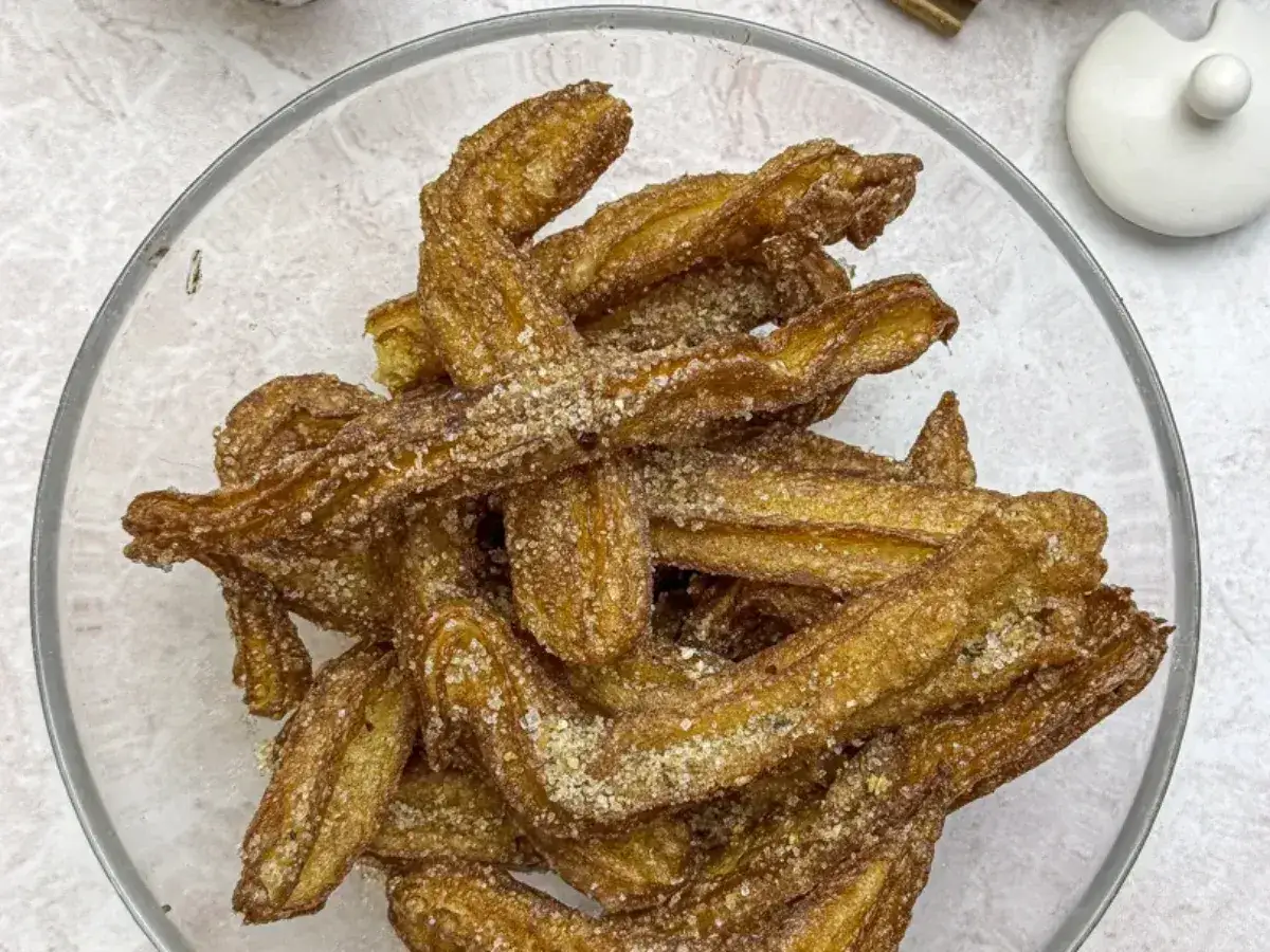 Churros co to? Złociste, chrupiące paluszki smażone i posypane cukrem z cynamonem, ułożone w szklanej misce.