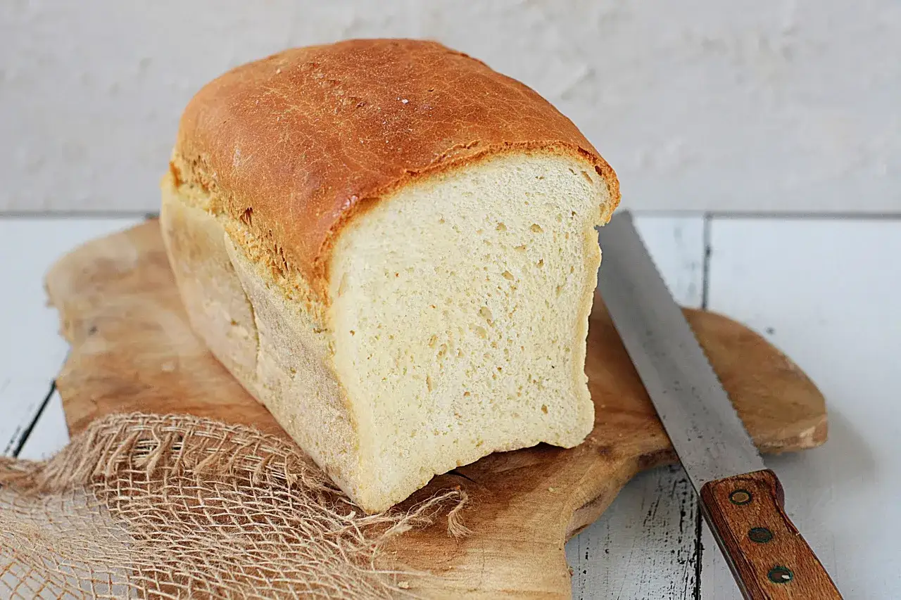 Świeżo upieczony chleb tostowy na desce, obok nóż do pieczywa. Idealny na poranne tosty.
