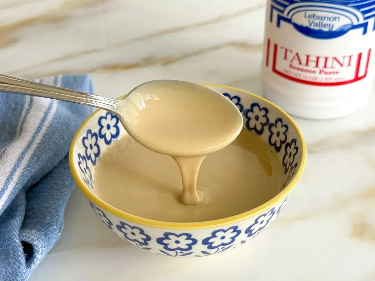 Gęsty, kremowy tahini, czyli pasta sezamowa, w miseczce. Obok słoik z napisem 