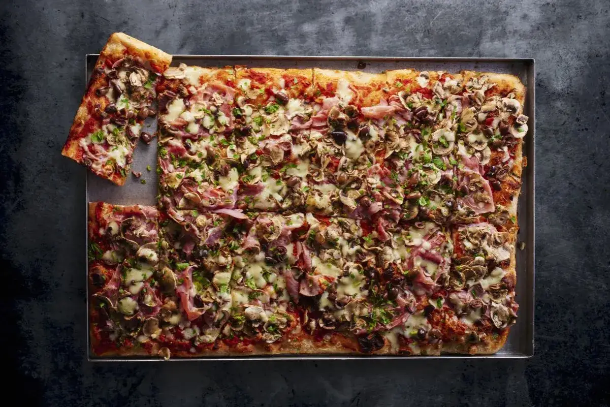 Pyszna pizza domowa przepis na blachę z szynką, pieczarkami i oliwkami. Idealna na rodzinne spotkanie.