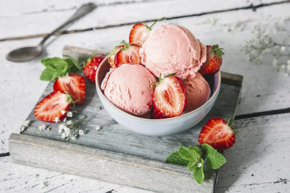 Pyszne lody truskawkowe w miseczce, ozdobione świeżymi truskawkami i miętą. Idealne na lato, jak zrobić lody truskawkowe?