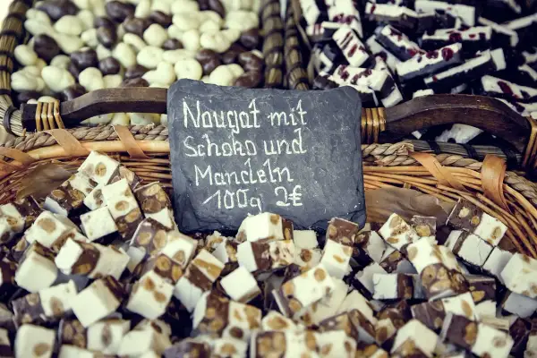 Kuszek nugatu z czekoladą i migdałami. Tabliczka informuje: "Nugat mit Schoko und Mandeln 100g 2€".