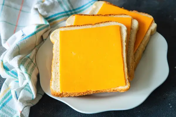 Gotowe do zrobienia pyszne tosty z airfryer. Trzy kromki chleba z serem cheddar na białym talerzyku.
