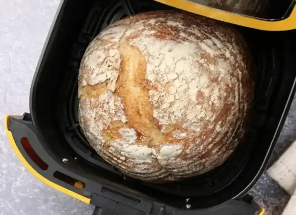 Chleb z airfryer, rumiany i lekko oprószony mąką, czeka na wyjęcie.