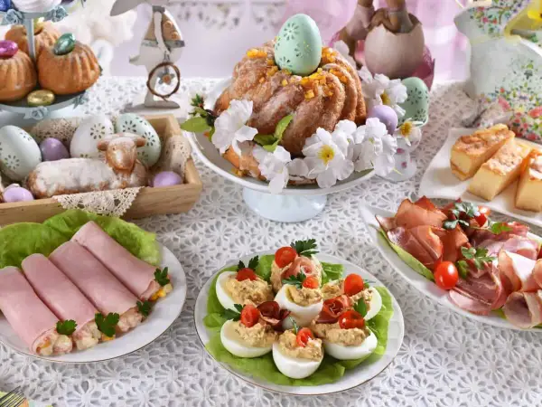 Udekorowany stół na śniadanie wielkanocne: babka, baranek, jajka faszerowane, wędliny i ciasto.