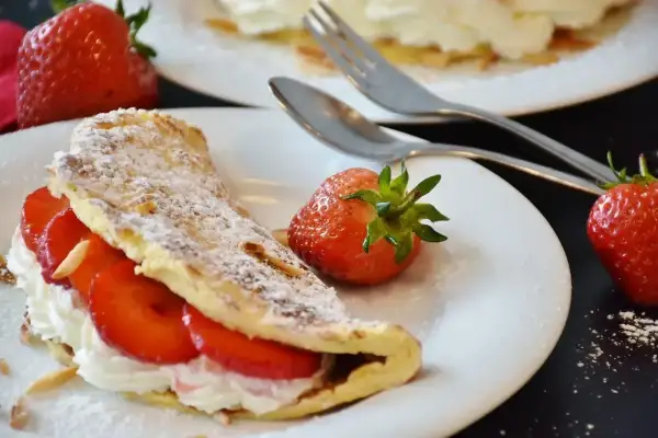Pyszny omlet z białek z bitą śmietaną i truskawkami, posypany cukrem pudrem i płatkami migdałów. Idealny deser.