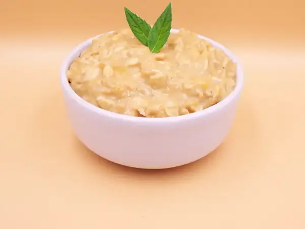 Pyszna owsianka z bananem, udekorowana listkami mięty, w białej miseczce na jasnym tle.