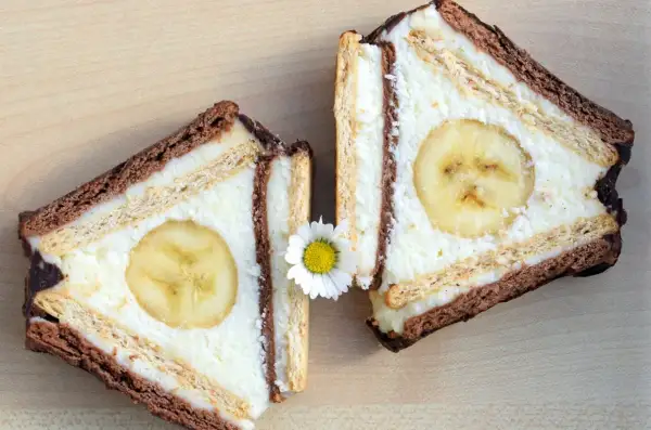 Dwa kawałki ciasta z sera z wiaderka, przypominające chatkę Puchatka, z bananem w środku i ozdobione stokrotką.