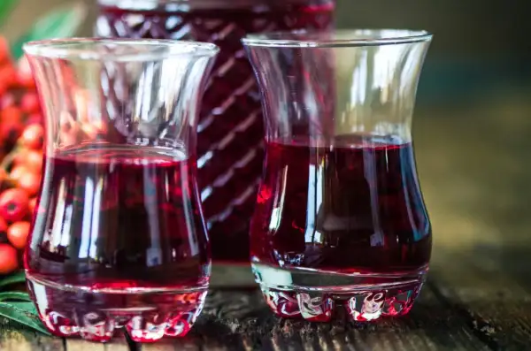 Dwa kieliszki wypełnione rubinową nalewką z czeremchy, obok butelka i kiść owoców.